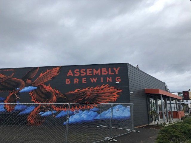 Assembly Brewing building with orange and black mural of a bird, gray exterior, cloudy sky.