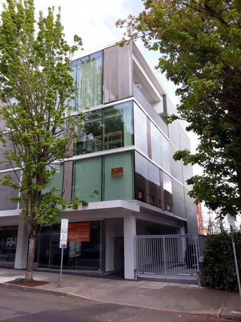 Modern building with glass walls and a white awning; trees frame the exterior.