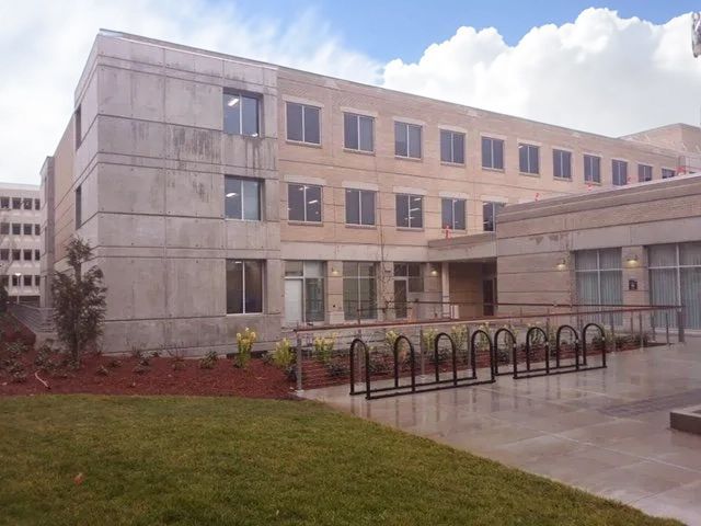 Gray and beige building with multiple windows, bike rack, and a small lawn.