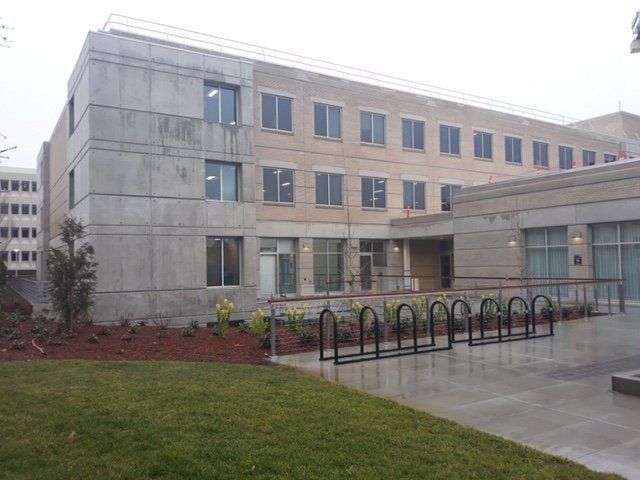 Gray and beige building with multiple windows, bike rack, and a small lawn.