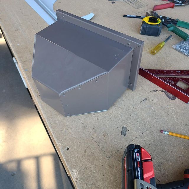 Brown metal gutter corner piece on a workbench with tools.