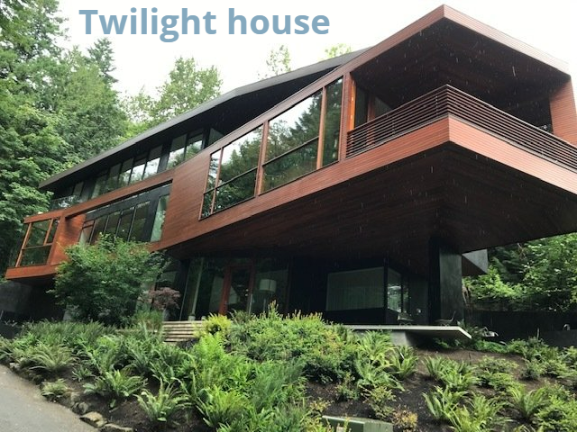 Modern brown house with large windows, built into a lush green hillside.