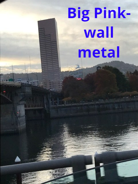 Tall pink skyscraper stands next to a river with a bridge in the distance; cloudy sky.