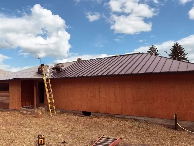 Metal roof being installed on a building, construction workers on roof, a ladder is present.