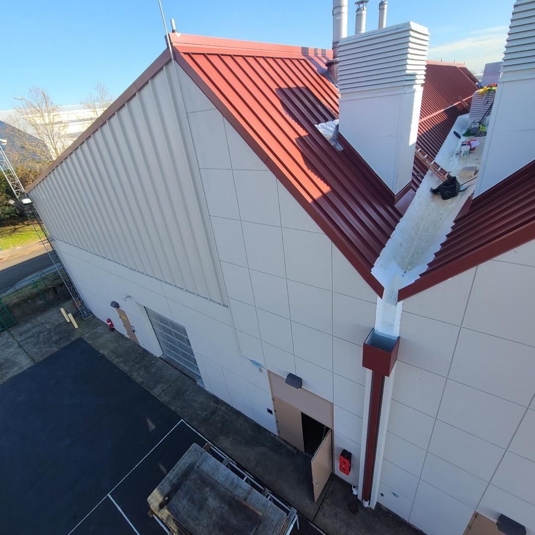 Modern industrial building exterior with gray and white facade under a blue sky with clouds.