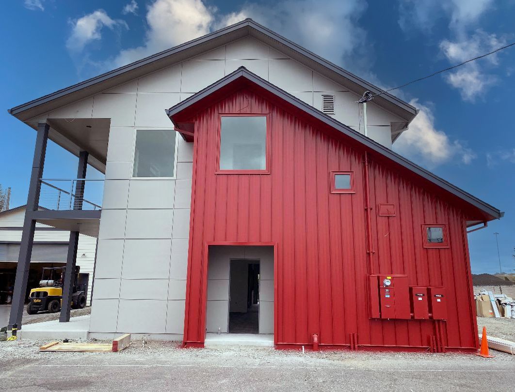 Modern building exterior with gray and red paneling; cloudy sky.