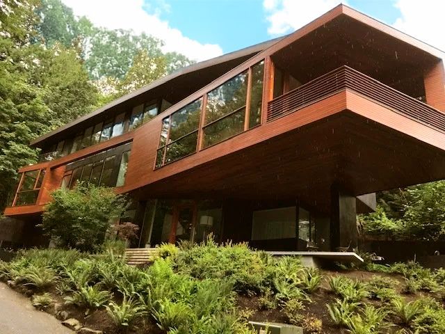 Modern brown house with large windows, built into a lush green hillside.