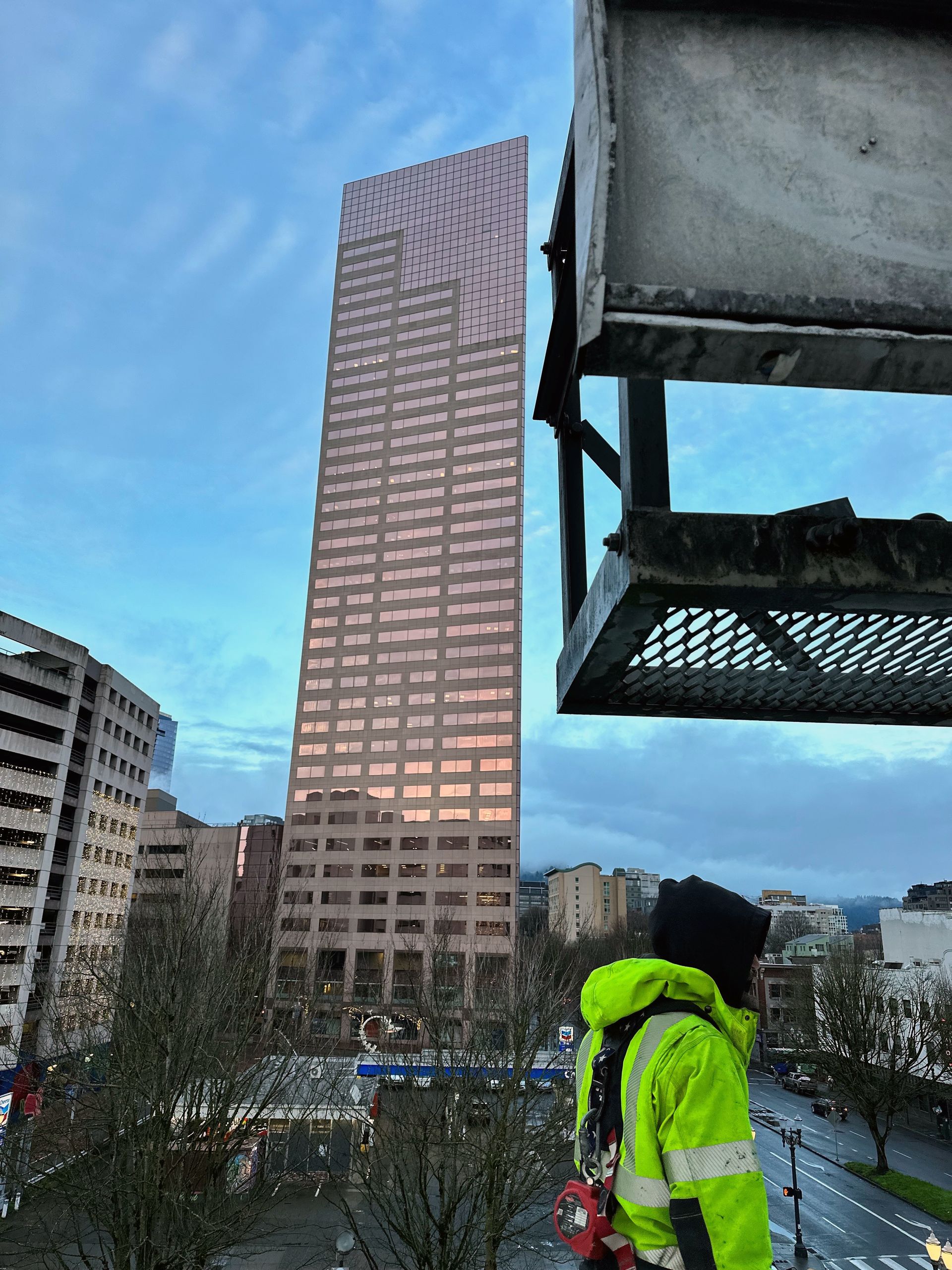 Tall pink skyscraper stands next to a river with a bridge in the distance; cloudy sky.