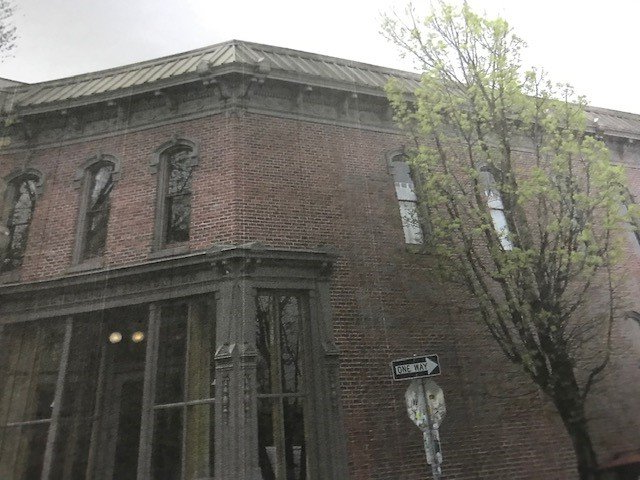 Brick building with ornate woodwork, corner view. Tree on the right, street sign in front. Overcast day.