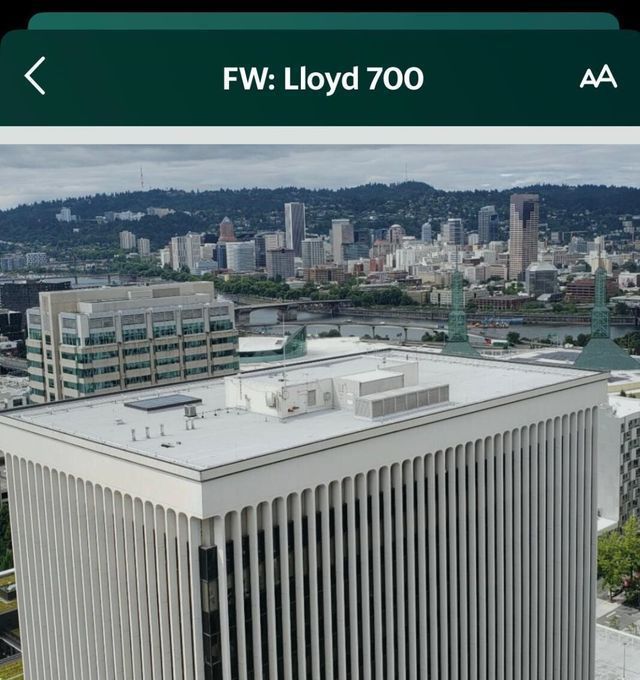 View of downtown buildings in Portland, Oregon from above; building facade in foreground, green hills in background.