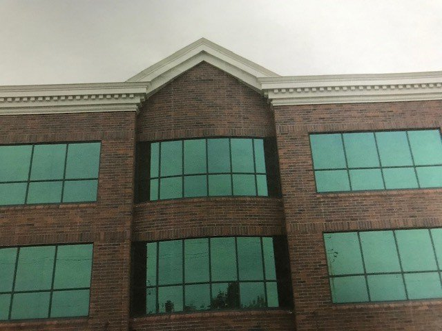 Brick building with teal-tinted windows under a white roof peak and trim, overcast sky.