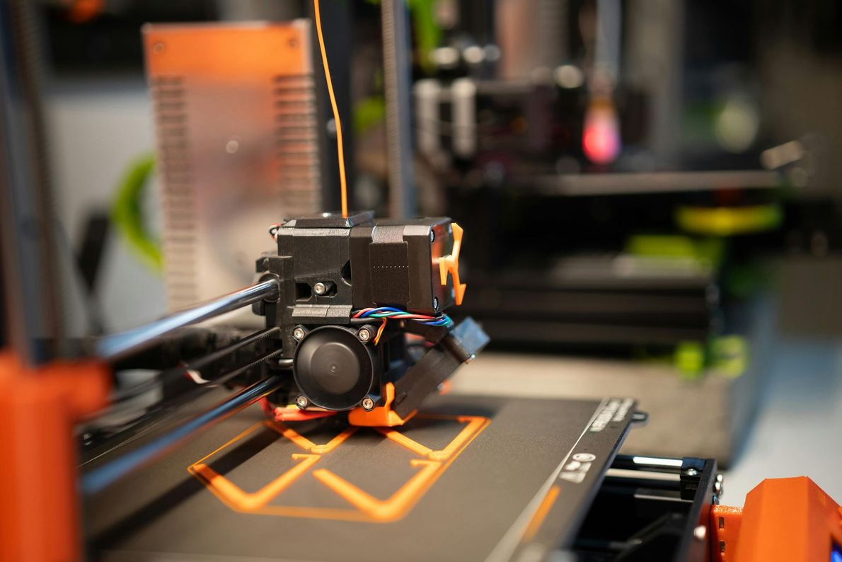 3D printer printing an orange object on the build plate