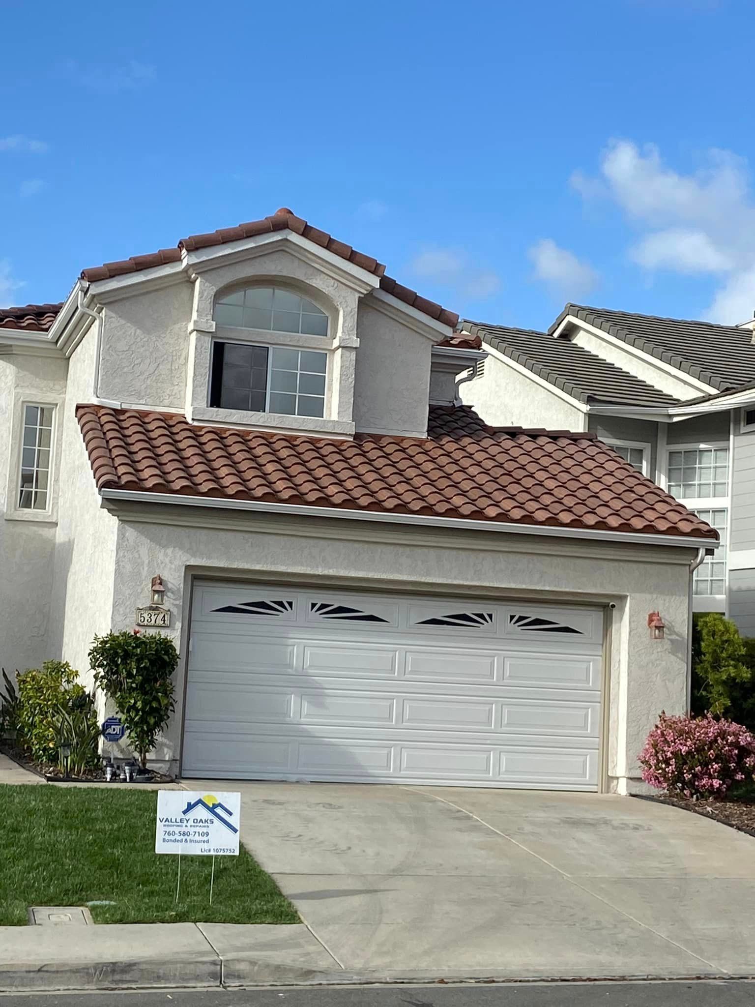 A white house with a red tile roof and a white garage door