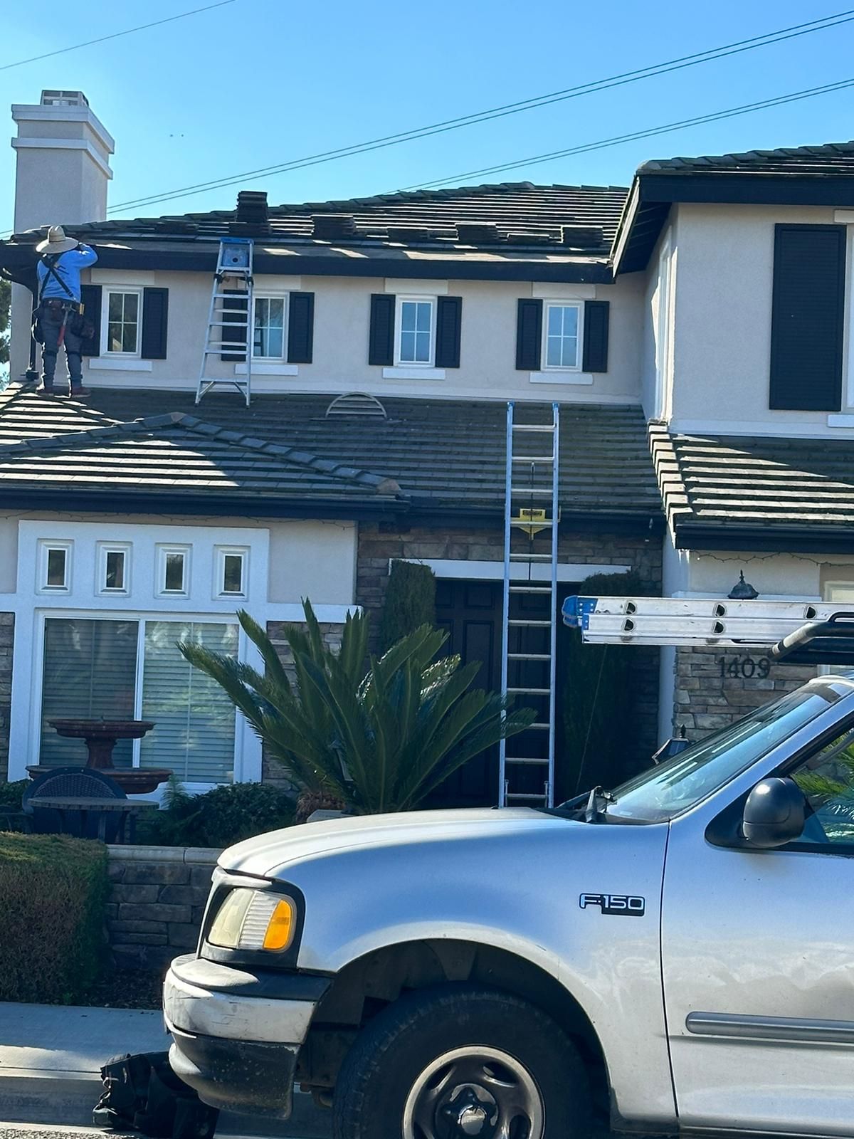 A white truck is parked in front of a house with a ladder on the roof.