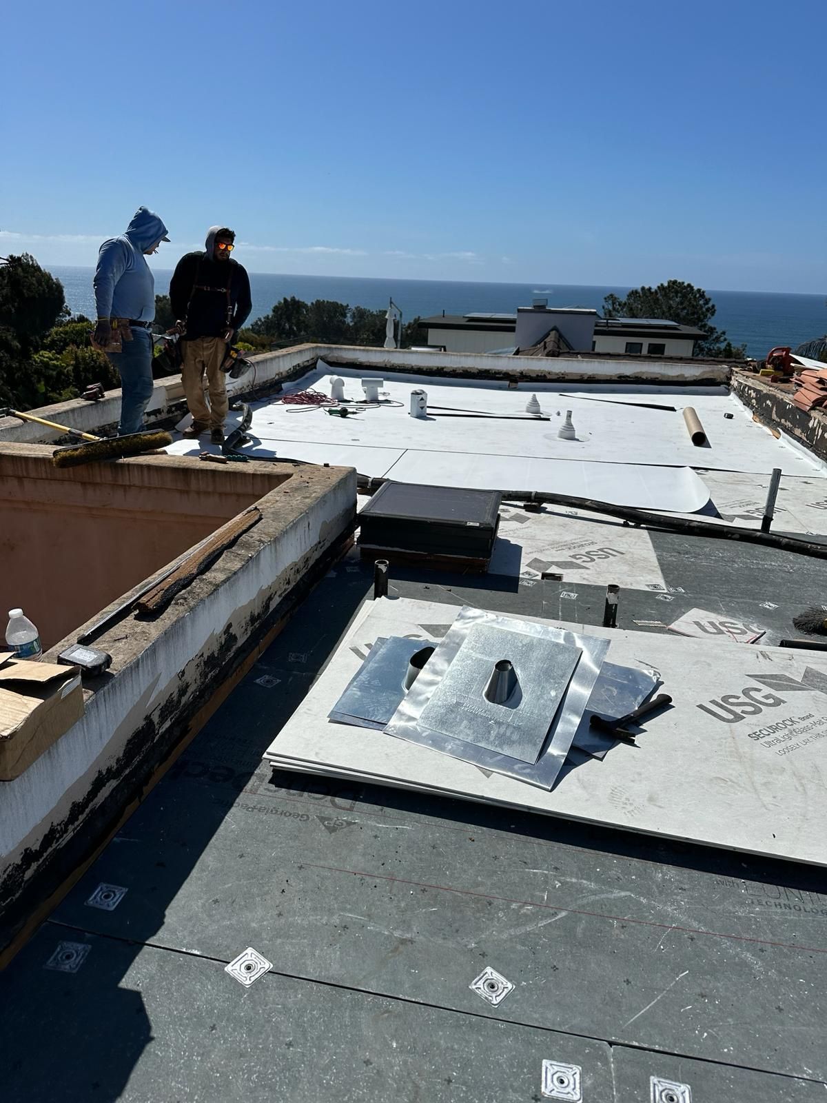 Two men are standing on top of a roof overlooking the ocean.