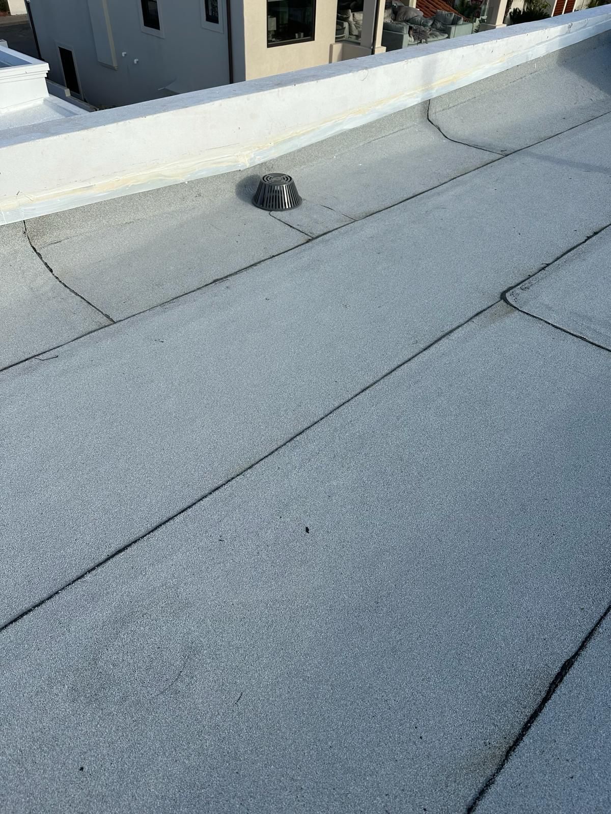 A roof with a drain on it and a building in the background.