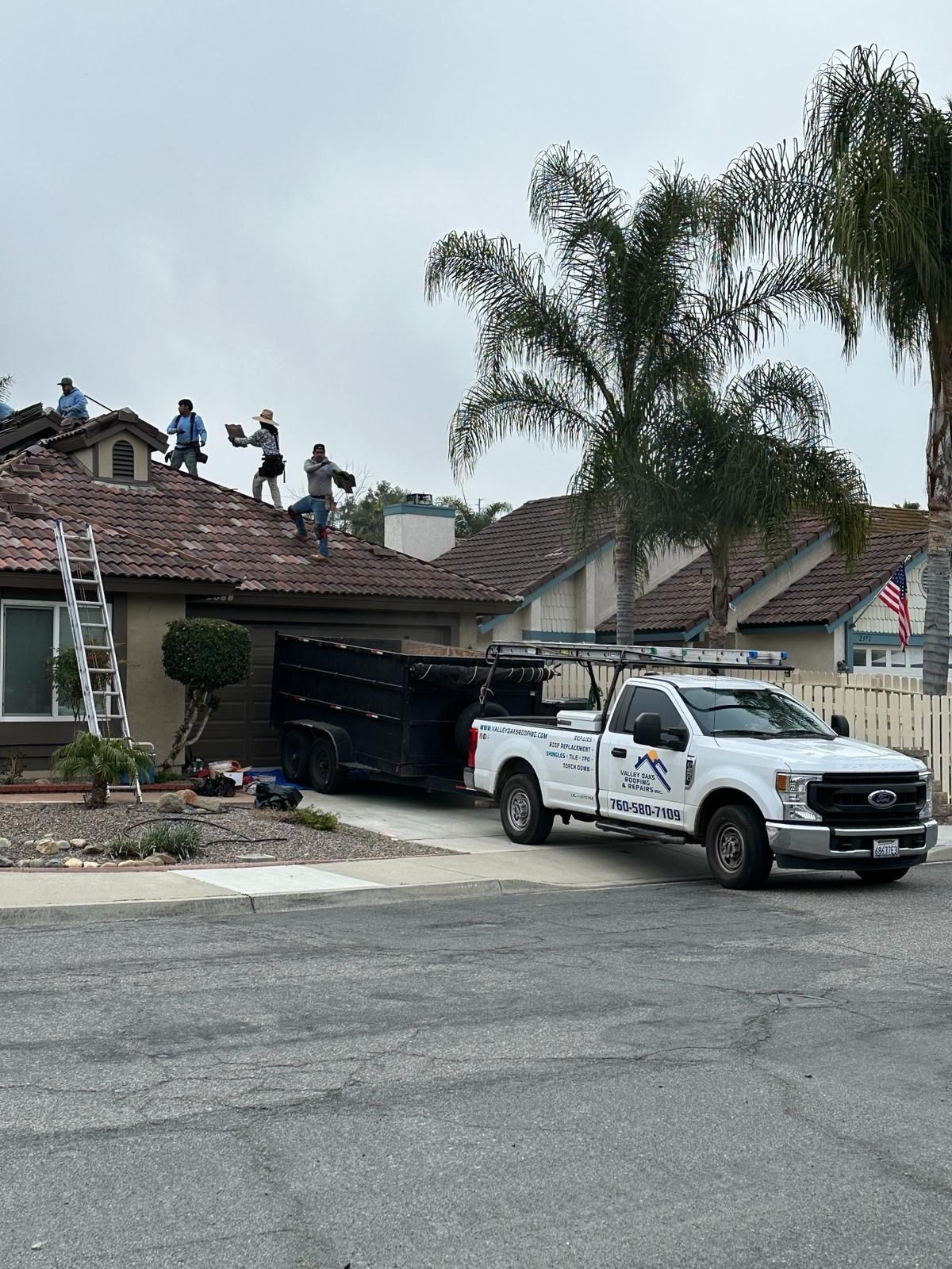 A white truck is parked in front of a house with people working on the roof.