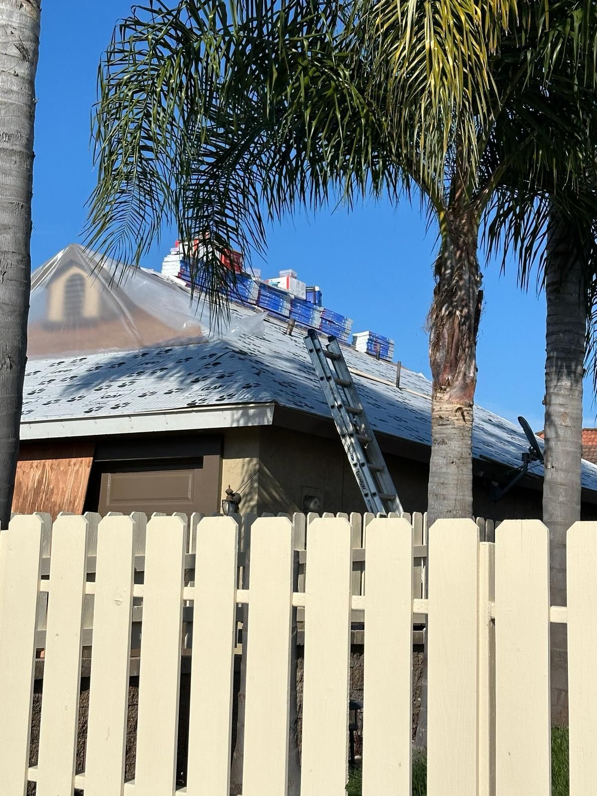 A white picket fence surrounds a house with a ladder on the roof.