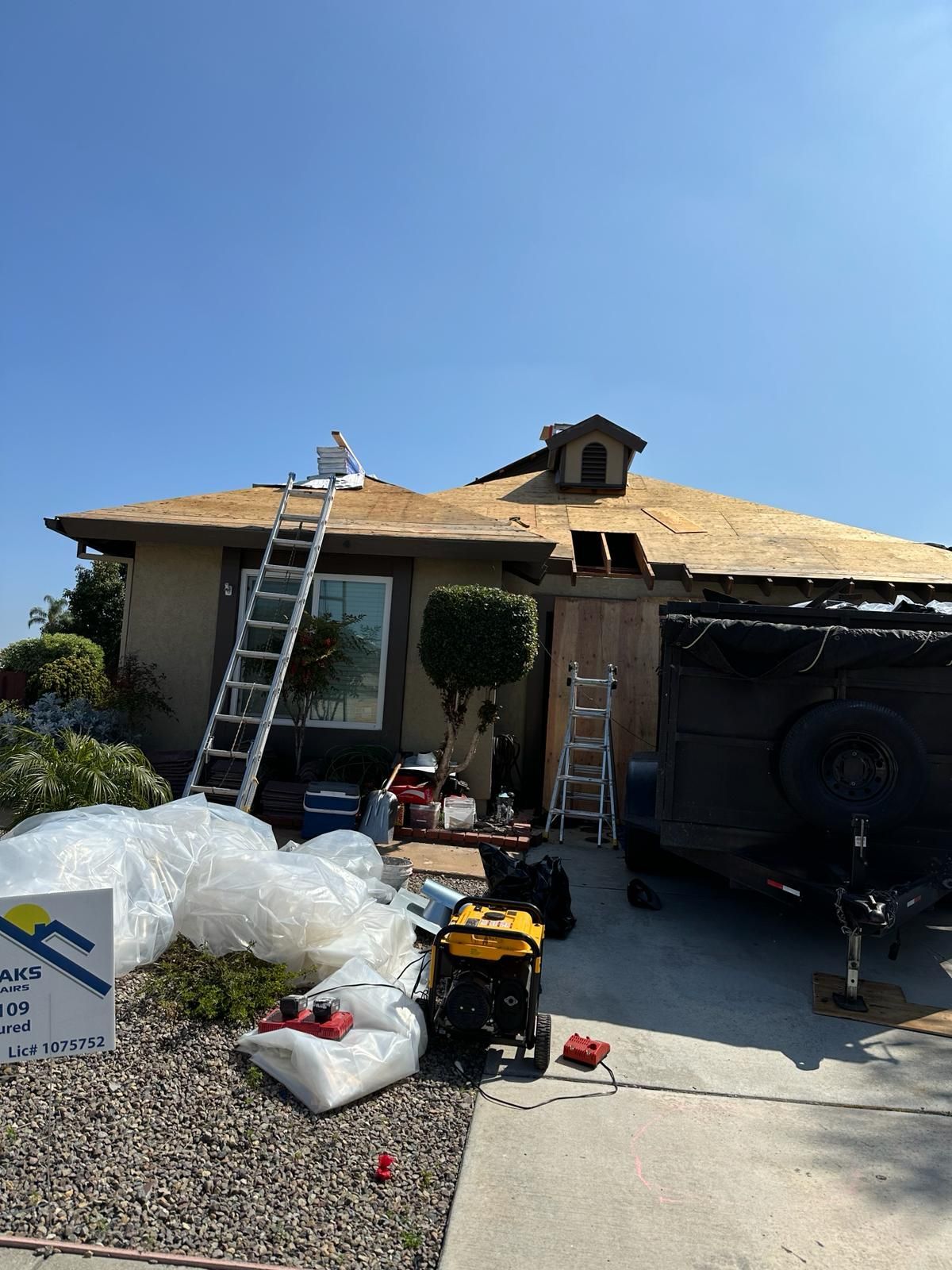 A man is standing on a ladder in front of a house that is being remodeled.