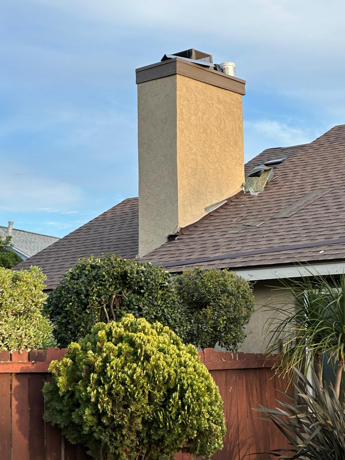 A chimney on the roof of a house next to a wooden fence.
