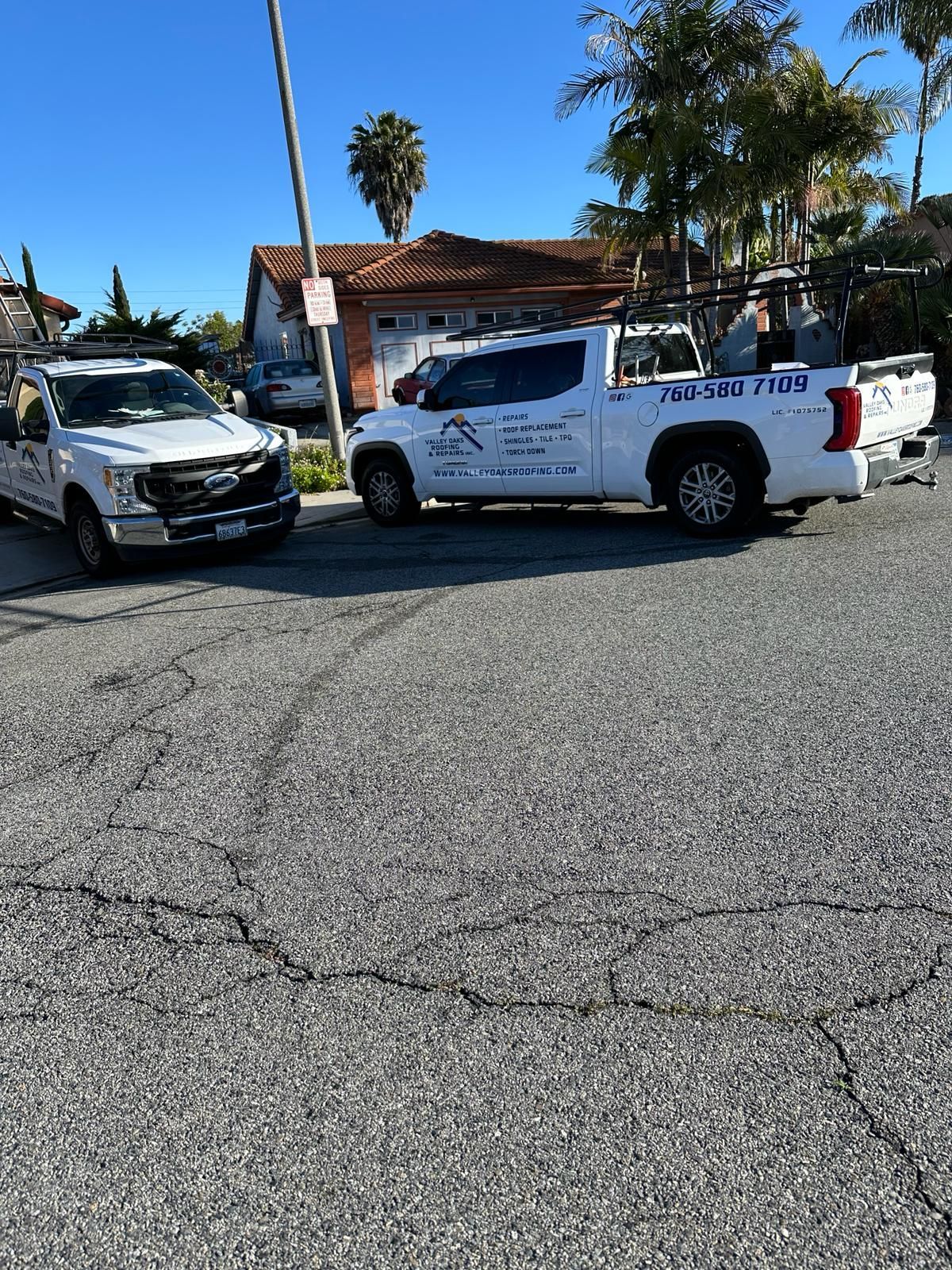 Two white trucks are parked on the side of the road.