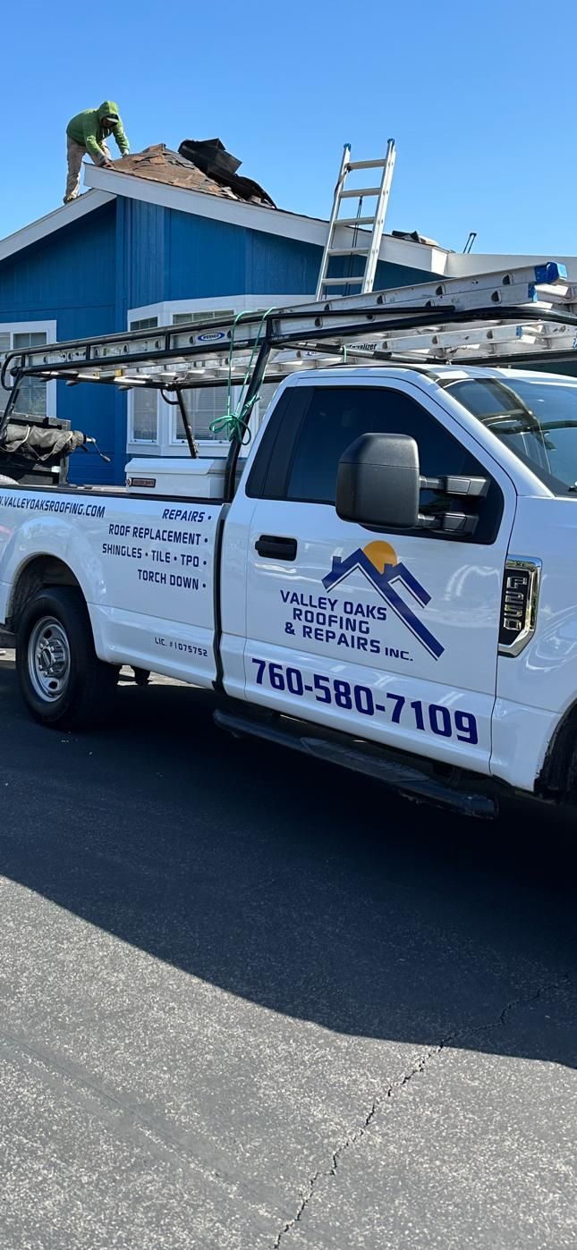 A white truck with a ladder on the back is parked on the side of the road.