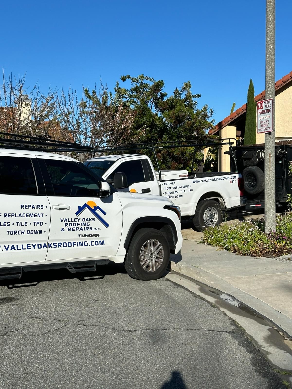 Two white trucks are parked on the side of the road.