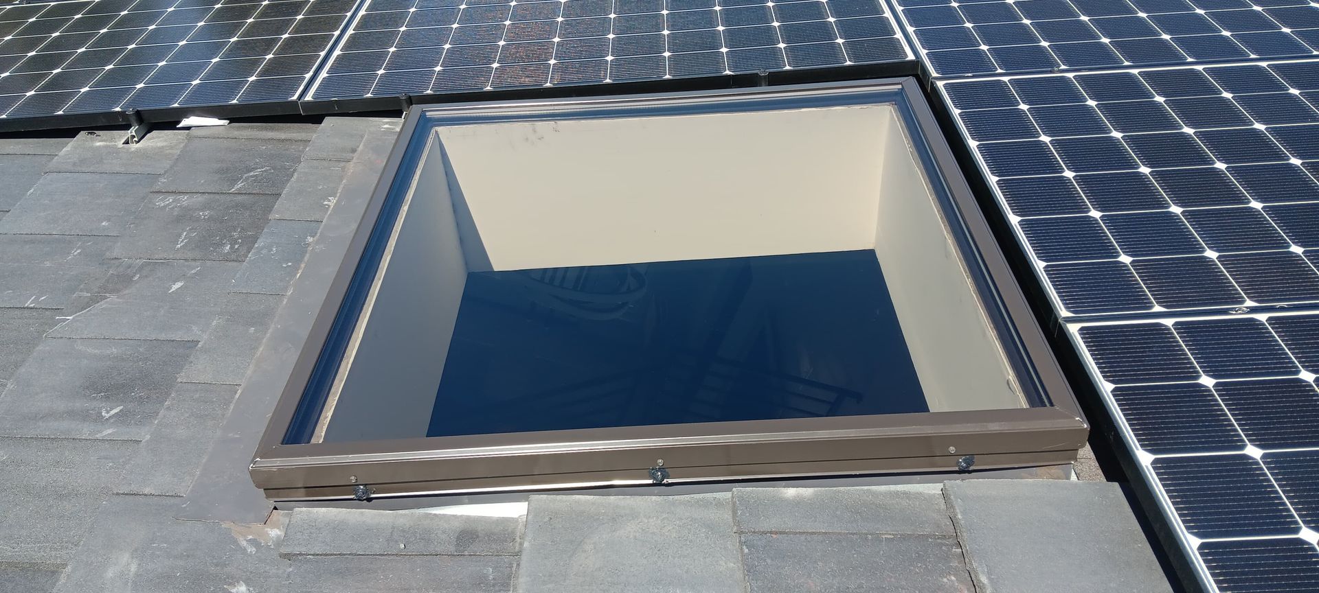 Skylight on a rooftop with solar panels. The skylight is open, allowing light in.