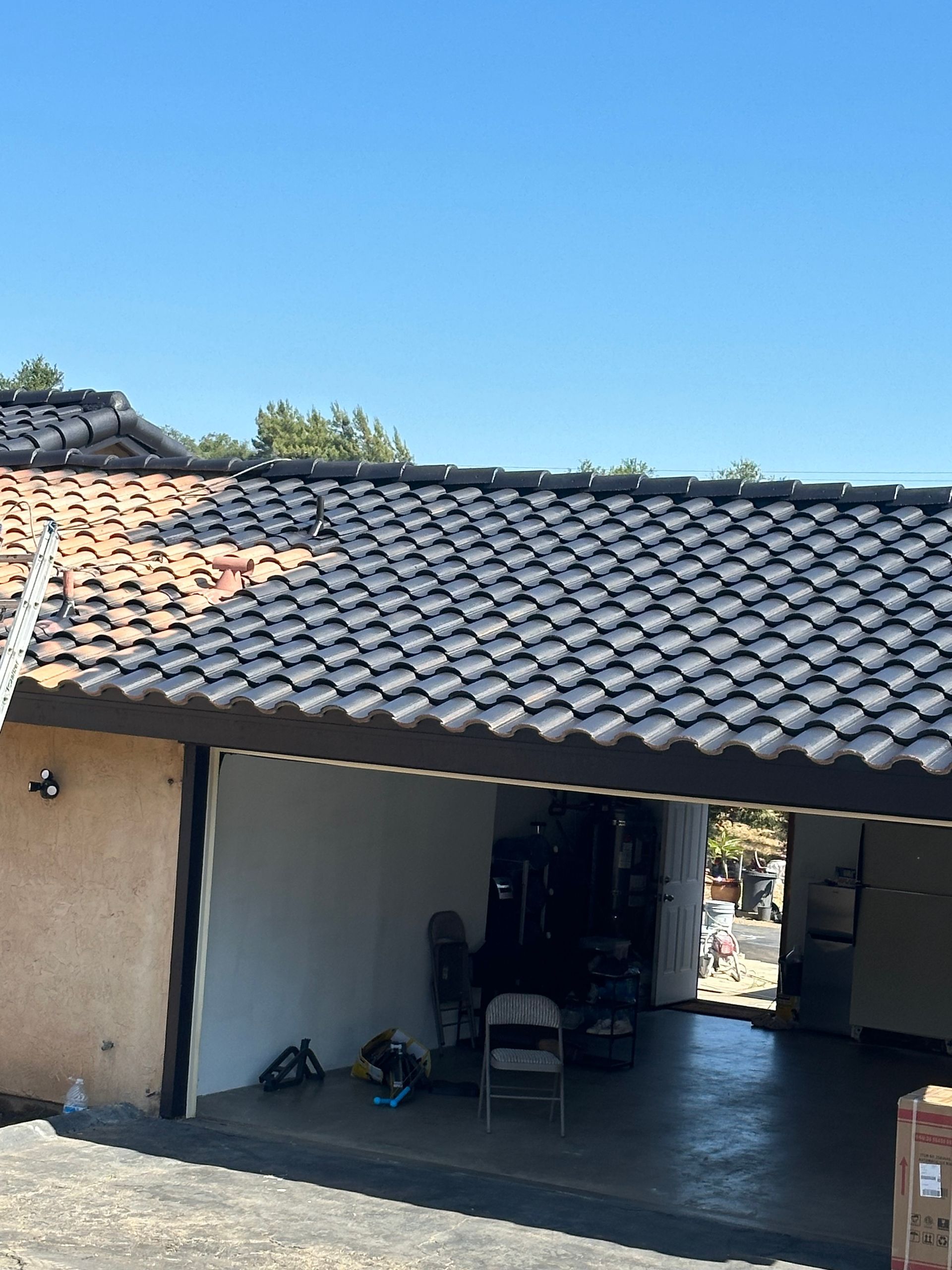 A partially re-roofed garage with black tiles next to older reddish-brown tiles under a blue sky.
