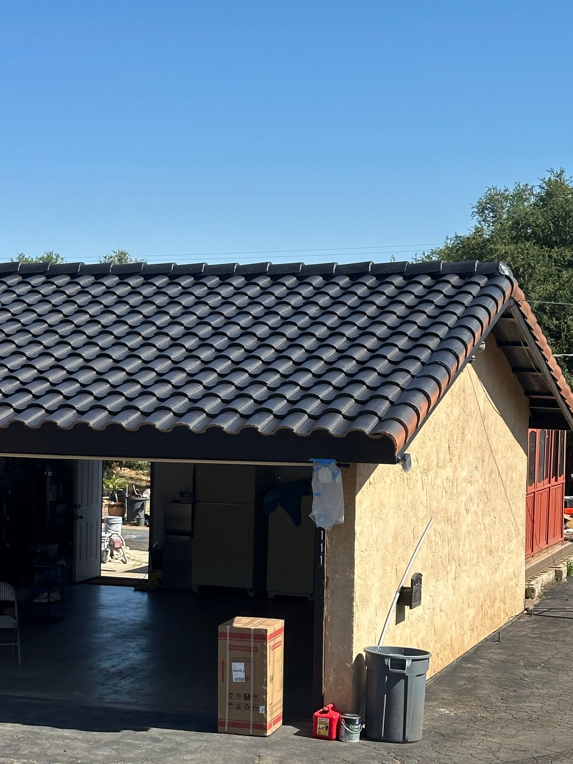 Tan stucco building with black tiled roof, open garage, and trash cans.