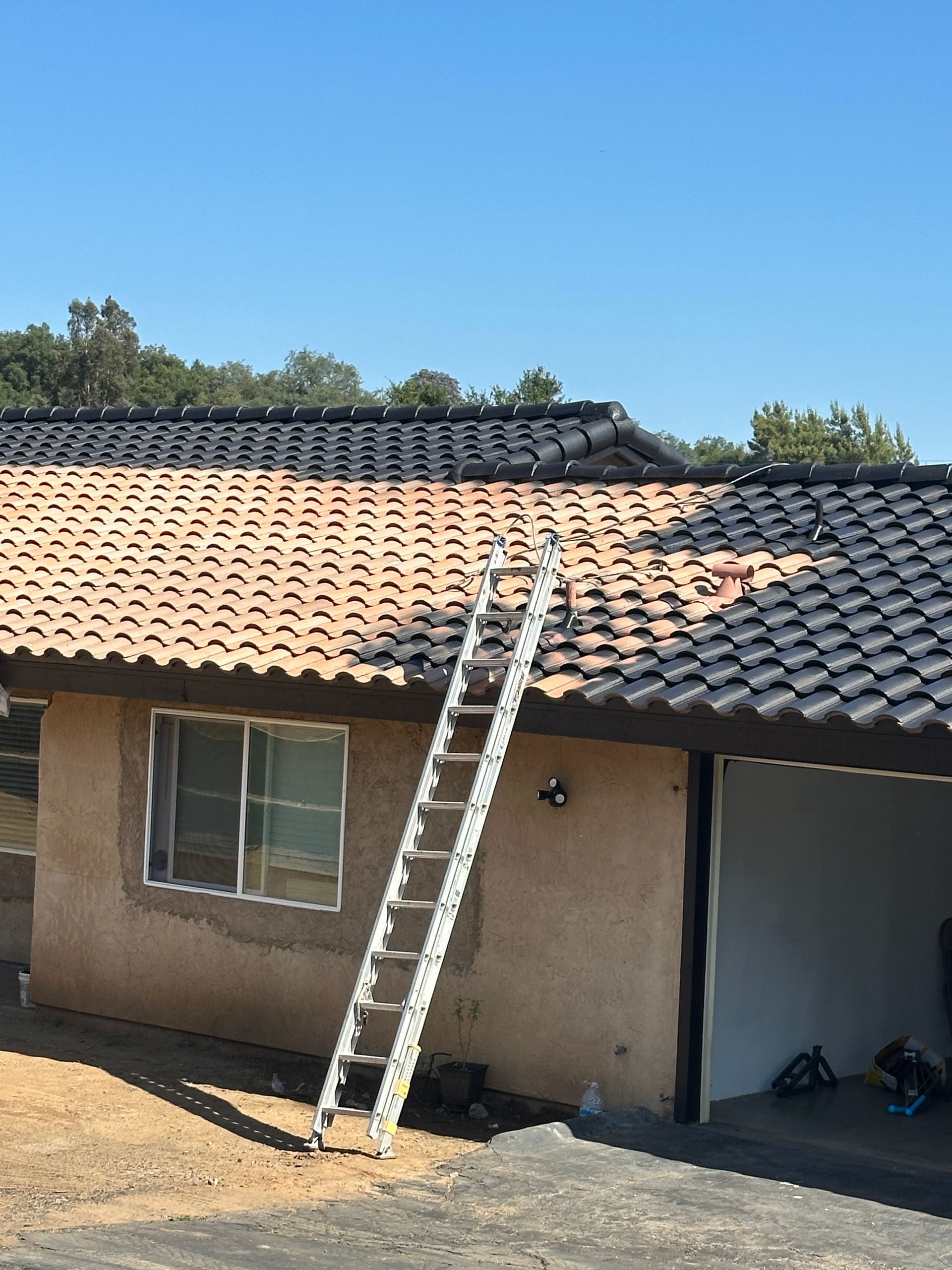 Ladder on a roof, half-painted black and the other half terracotta, on a sunny day.