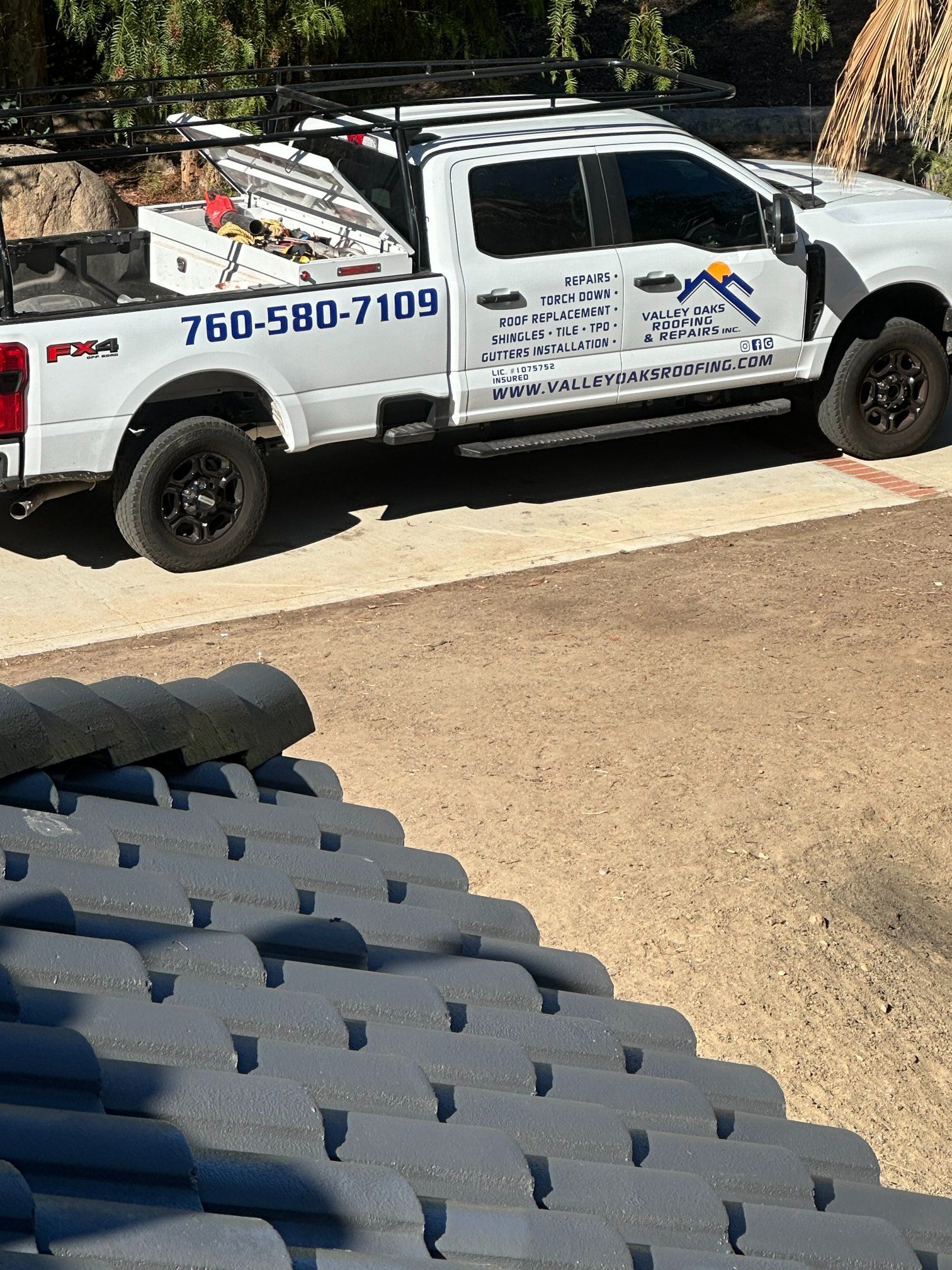 White work truck with tools parked on a driveway next to a terracotta tiled roof.