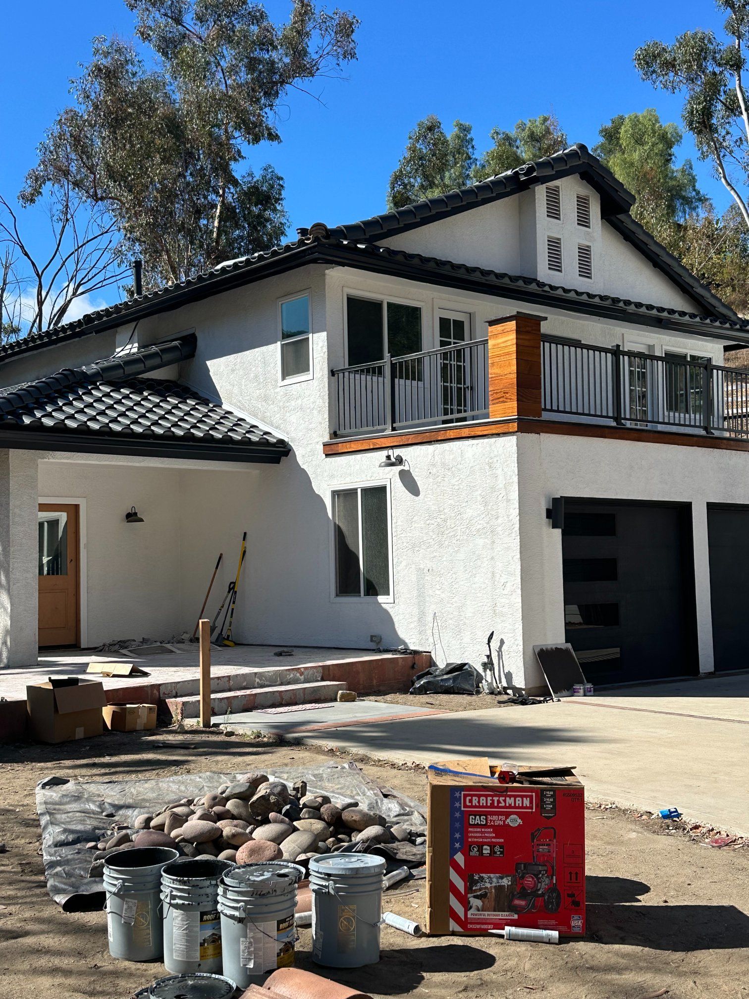 Two-story white stucco house under construction with a black tile roof and a balcony.