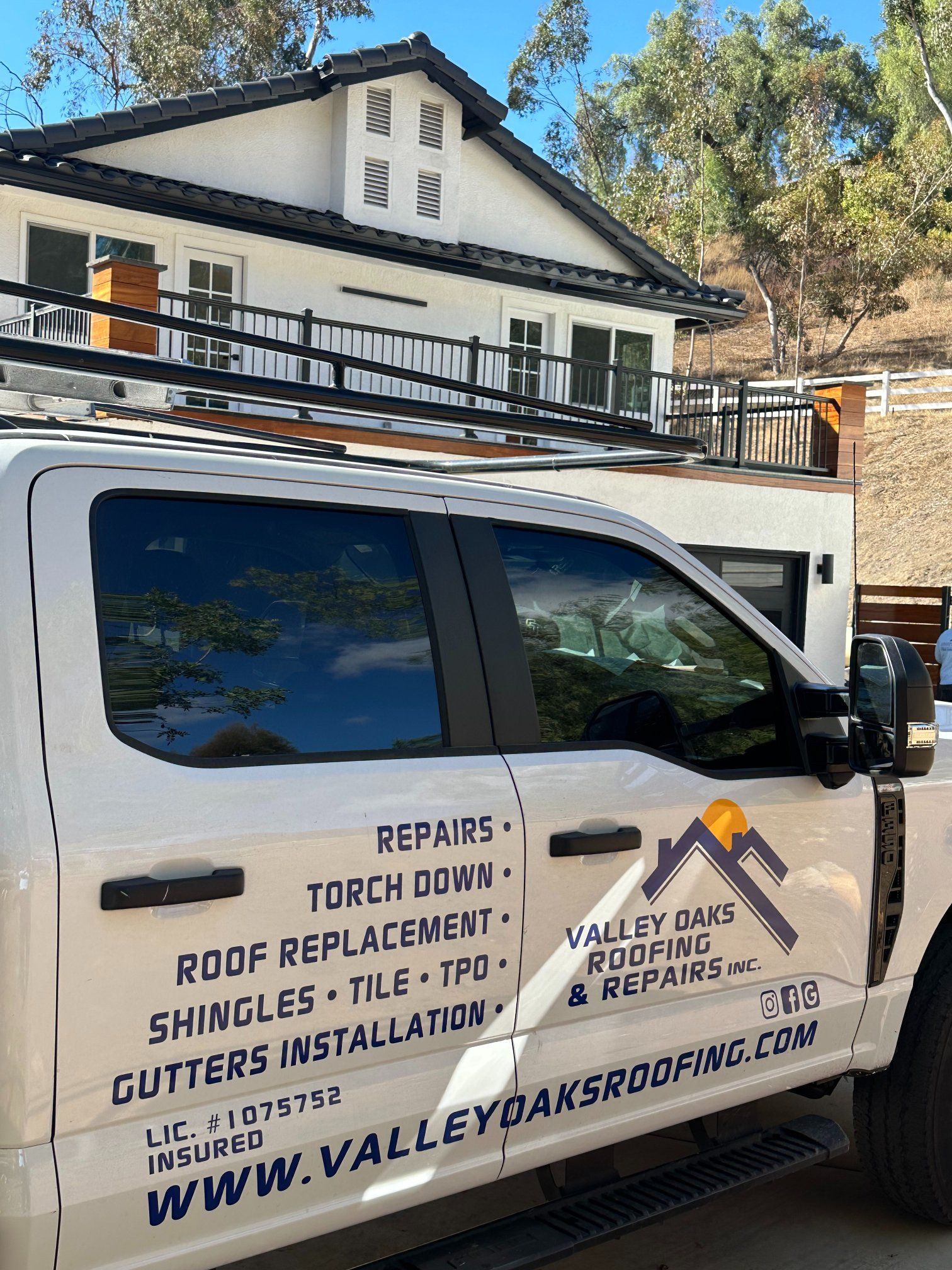 White truck with roofing company logo parked in front of a house, advertising repairs and services.