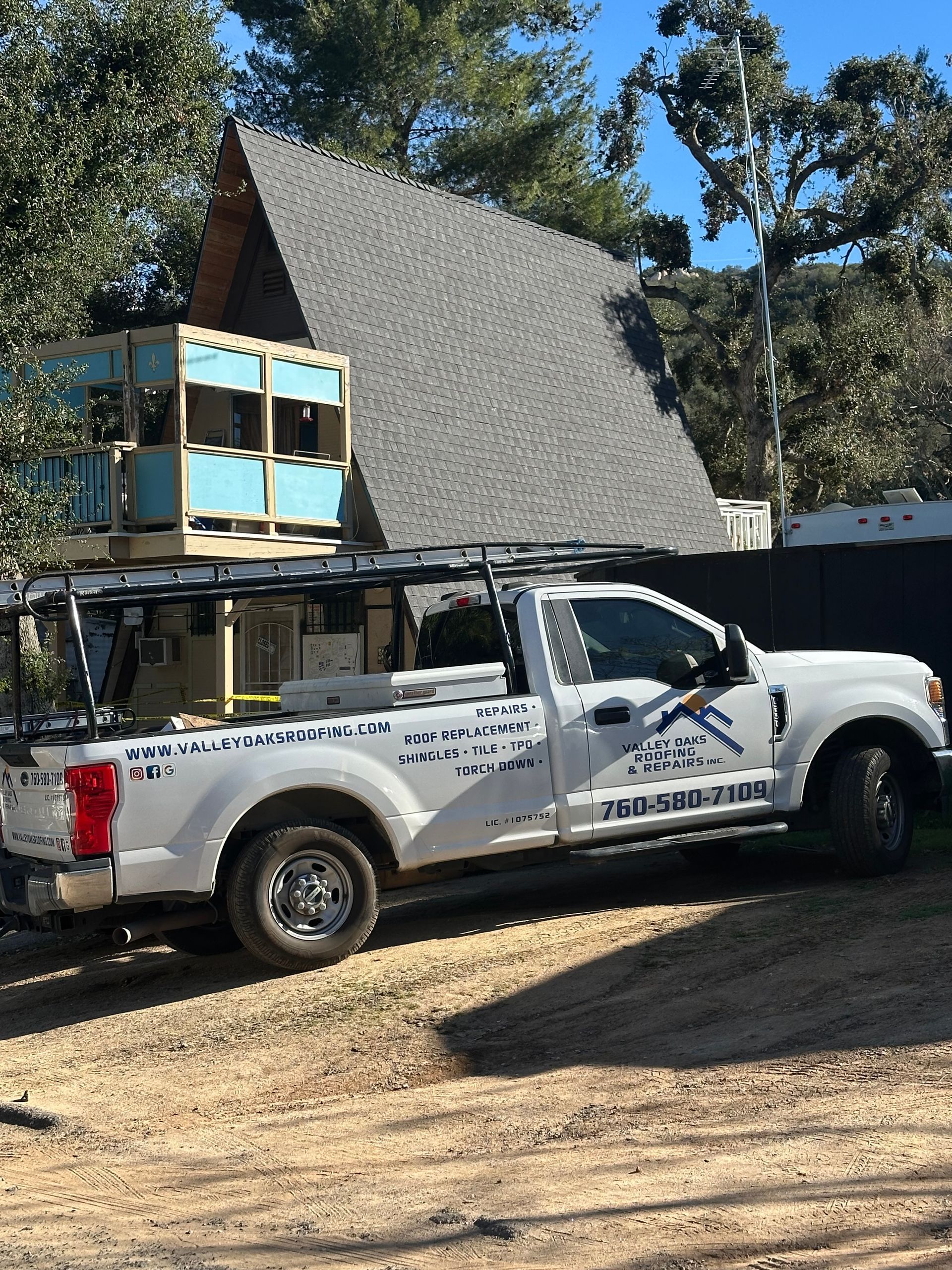 White pickup truck with a rack, blue wooden structure on top, A-frame house in the background.