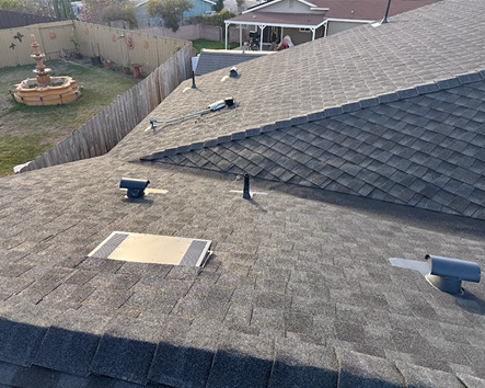 Dark shingle roof with vents, a skylight, and a backyard with a fountain.