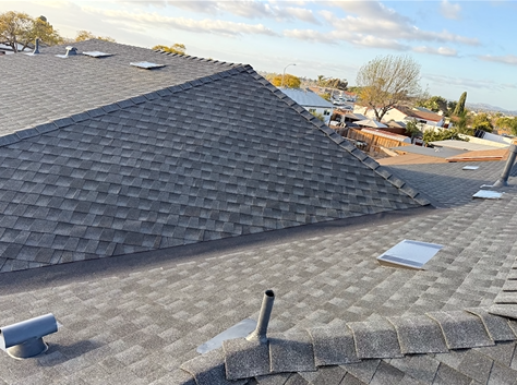 Gray shingled rooftop with vents, overlooking a residential neighborhood on a sunny day.