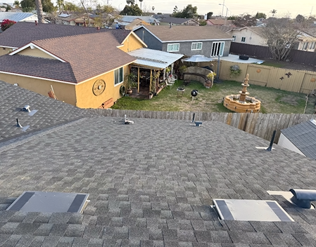 View of a residential neighborhood with newly shingled roof in the foreground and homes with yards in the background.