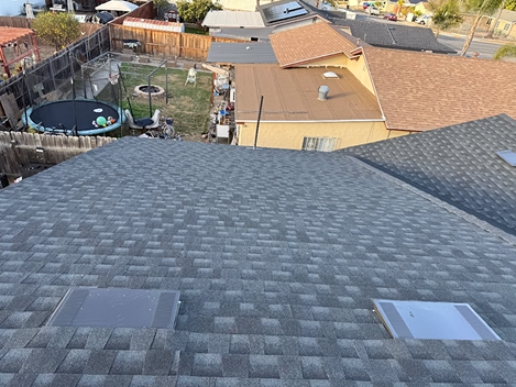 Overhead view of a gray shingled roof with skylights; backyard and neighboring houses visible.