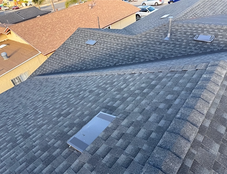 Overhead view of a gray shingle roof with skylights. Another brown roof visible to the left.