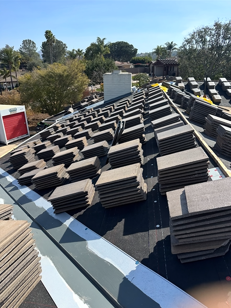 Roof tiles stacked on a roof under construction, with a clear blue sky.