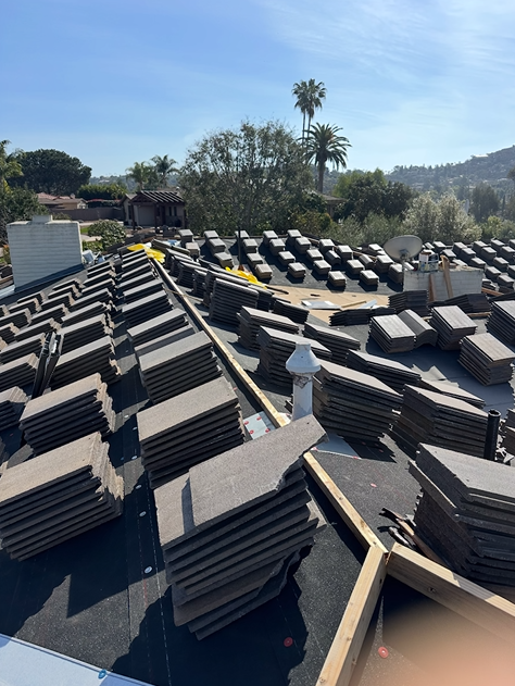 Roofers installing new gray tiles on a house roof on a sunny day.