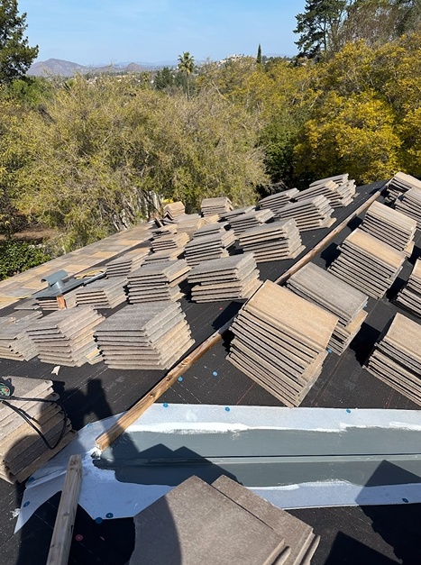Roof with stacks of beige tiles, overlooking green trees.