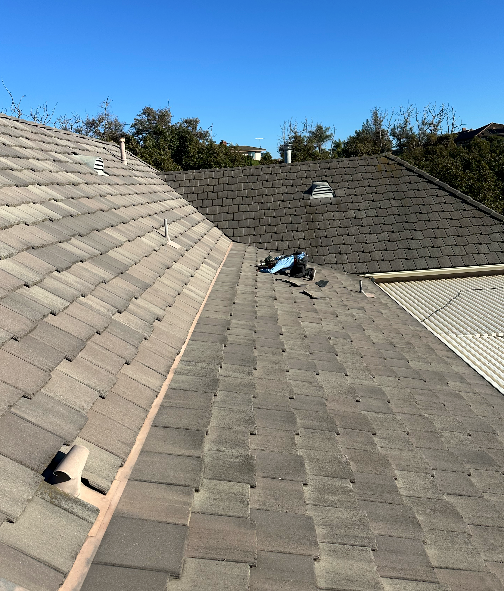 Rooftop view with brown tile shingles, clear blue sky, and visible construction tools.