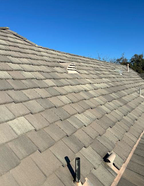 Gray tiled roof under a clear blue sky; vents and pipes visible.