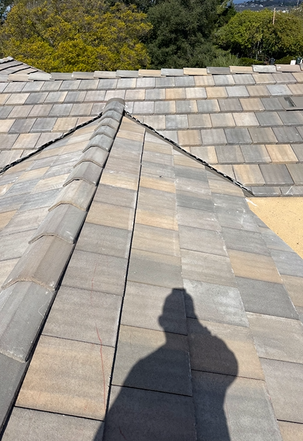 Gray and tan tile roof, sunny day, with person's shadow.