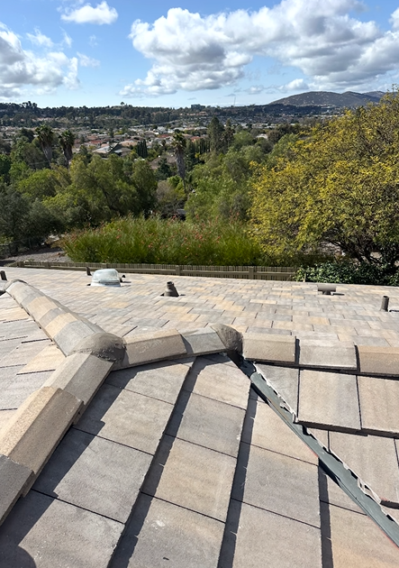 View from a tile roof overlooking a green valley and distant hills under a partly cloudy sky.