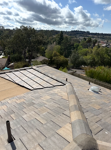 Rooftop view overlooking a residential area. Partially replaced roof with tile, brown and tan hues. Cloudy sky.