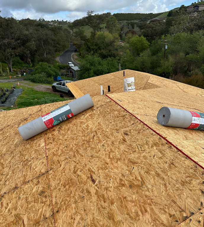 New roof construction: rolls of gray underlayment on oriented strand board, with a bucket.