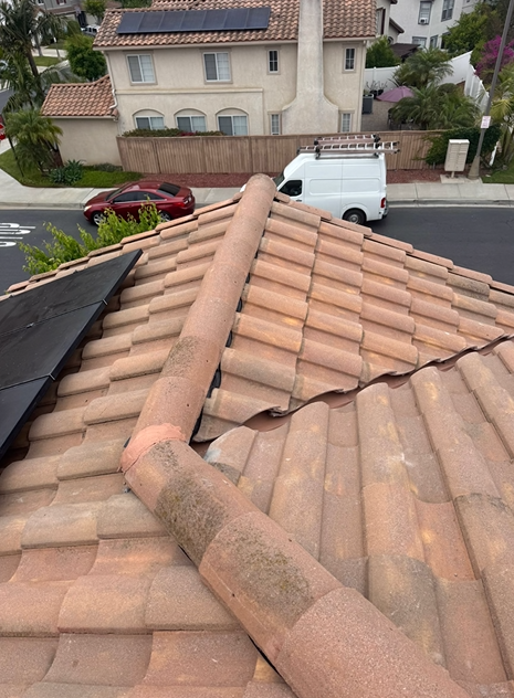 Terracotta tile roof with curved vent pipe, solar panel, street and houses in background.